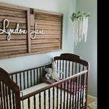 white wooden name sign above crib on nursery wall